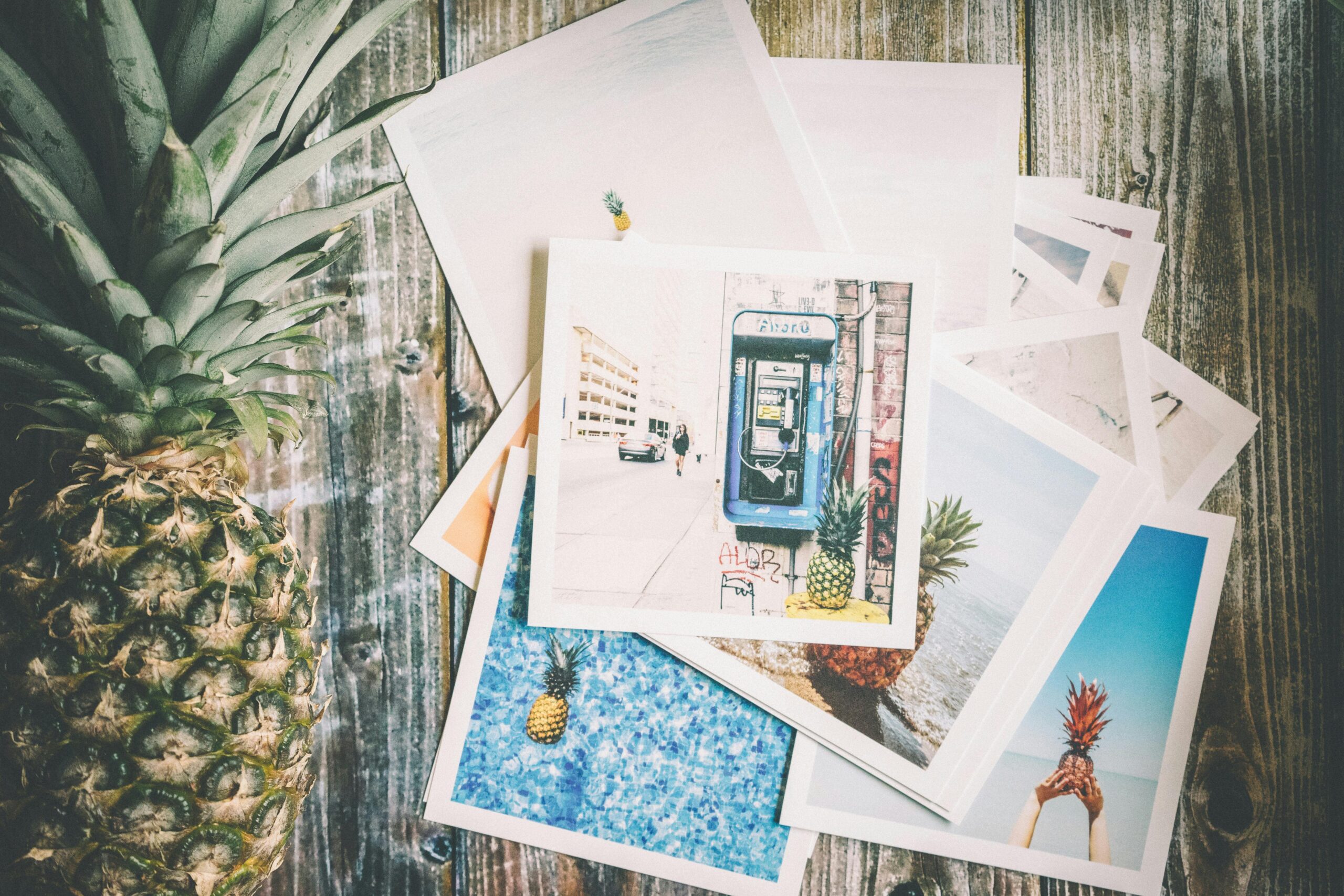 An artistic collection of travel-themed photos with a pineapple on rustic wood.