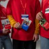 Volunteers in red shirts holding informational booklets on art and eco volunteering.